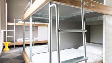 Habitación con literas de metal, cabeceros de madera y una silla amarilla.