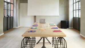 Un salón de conferencias con una larga mesa, sillas, una pantalla de proyector y un ordenador portátil.