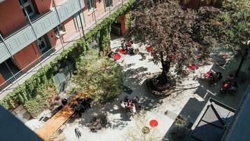 Ein Innenhof mit Sitzbereichen, einem zentralen Baum und einem Gebäude mit Balkonen.