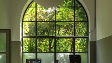 Ein Fitnessstudio mit Laufband, Ergometer und einem großen Bogenfenster mit Blick auf eine grüne Landschaft.