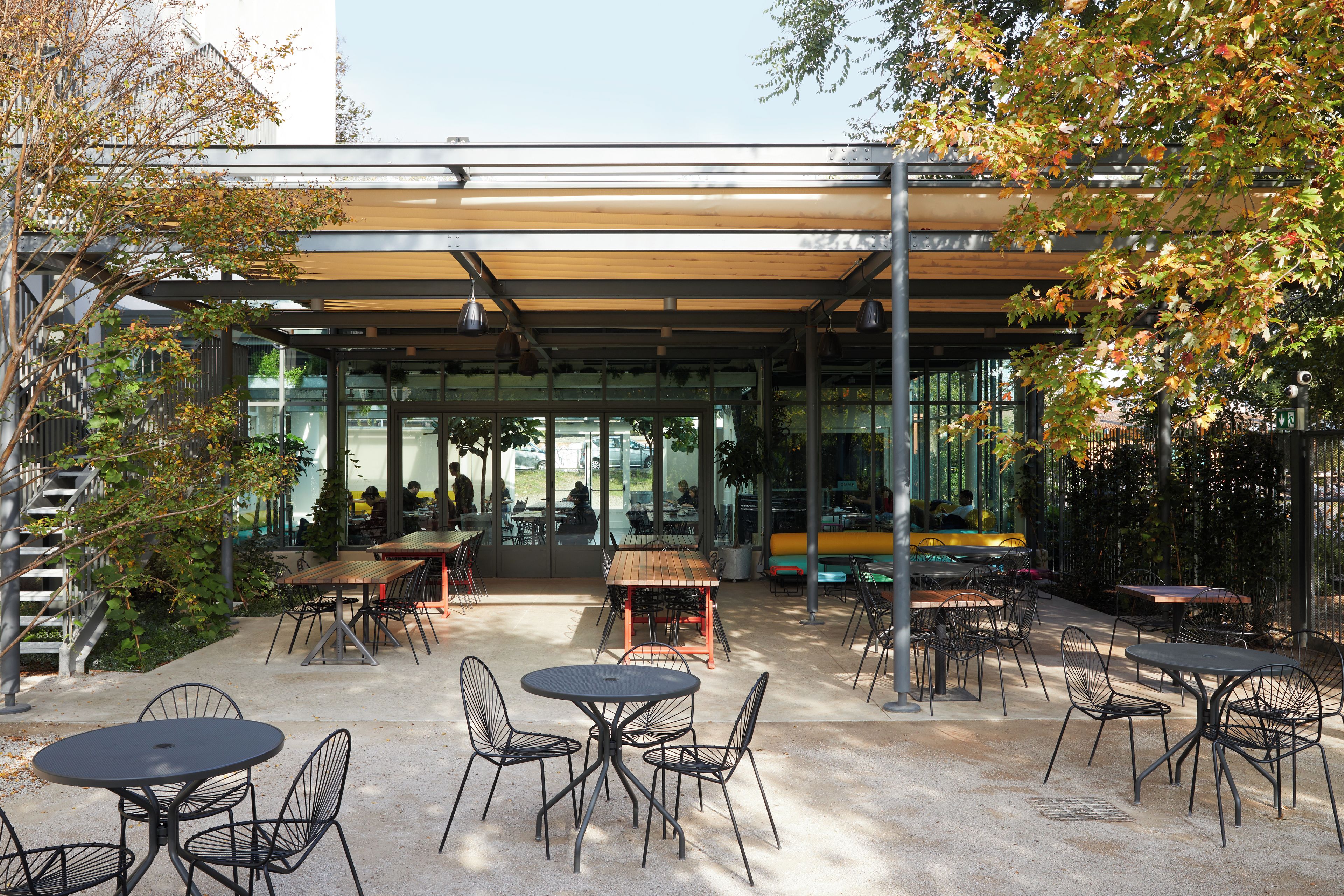 An outdoor cafe with tables and chairs, a covered seating area, and a view of the street.