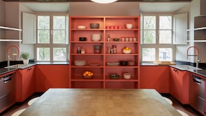 Una cocina moderna con armarios rojos, una isla central y estanterías empotradas con diferentes utensilios de cocina.