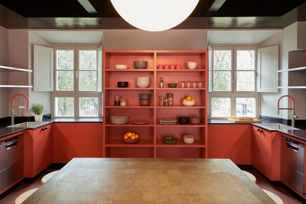 A modern kitchen with red cabinetry, a central island, and built-in shelves with various kitchenware. - Combo Milano - Hostel (Milan)