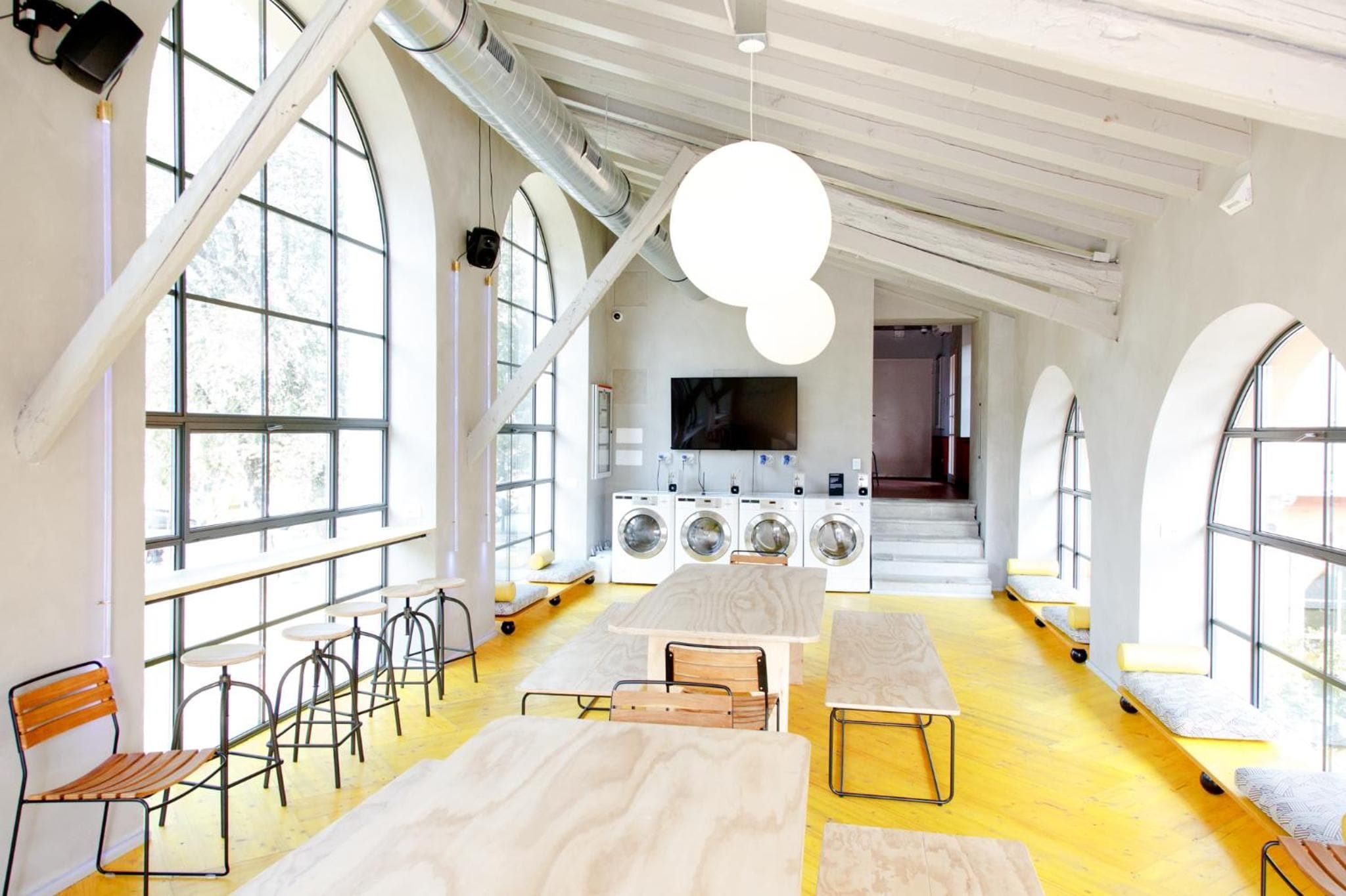 A spacious room with large windows, a flat-screen TV, a washing machine, and a seating area with stools and benches.
