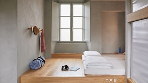 Una habitación minimalista con suelo de madera, una ventana, una cama, un banco y una colchoneta de yoga.