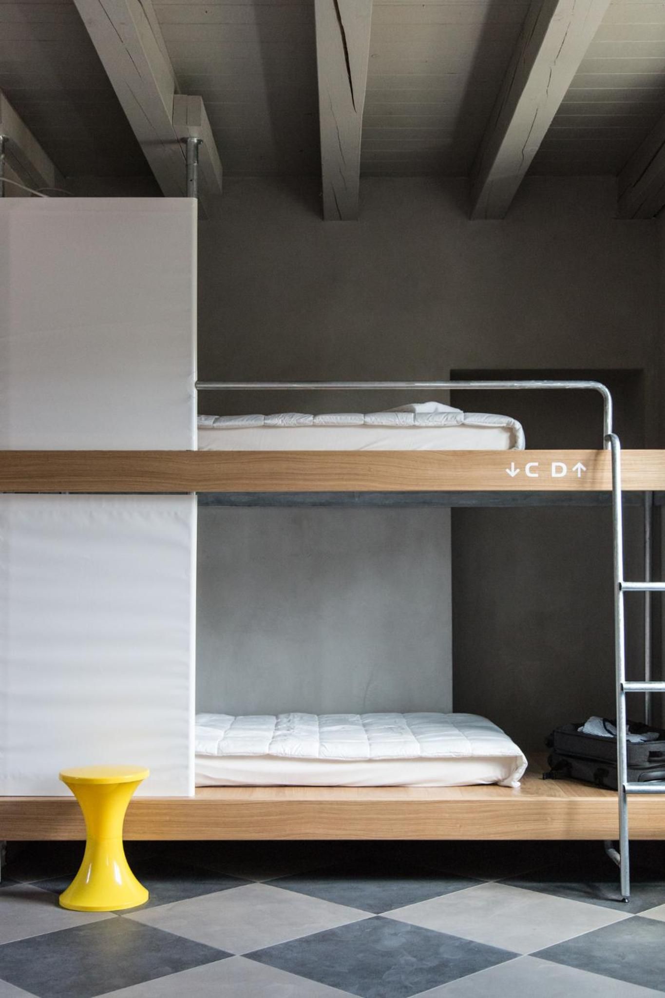 Una cama litera con una escalera, un taburete amarillo pequeño y un colchón en la cama inferior.
