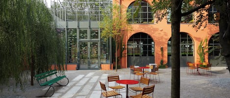 An outdoor seating area with tables and chairs, a green bench, and a glass building with fish decorations.