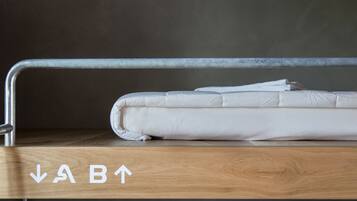 Una cama individual con estructura metálica, plataforma de madera y flechas que indican la orientación de la cama.
