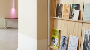 Una estantería de madera con libros y una lámpara vertical rosa.