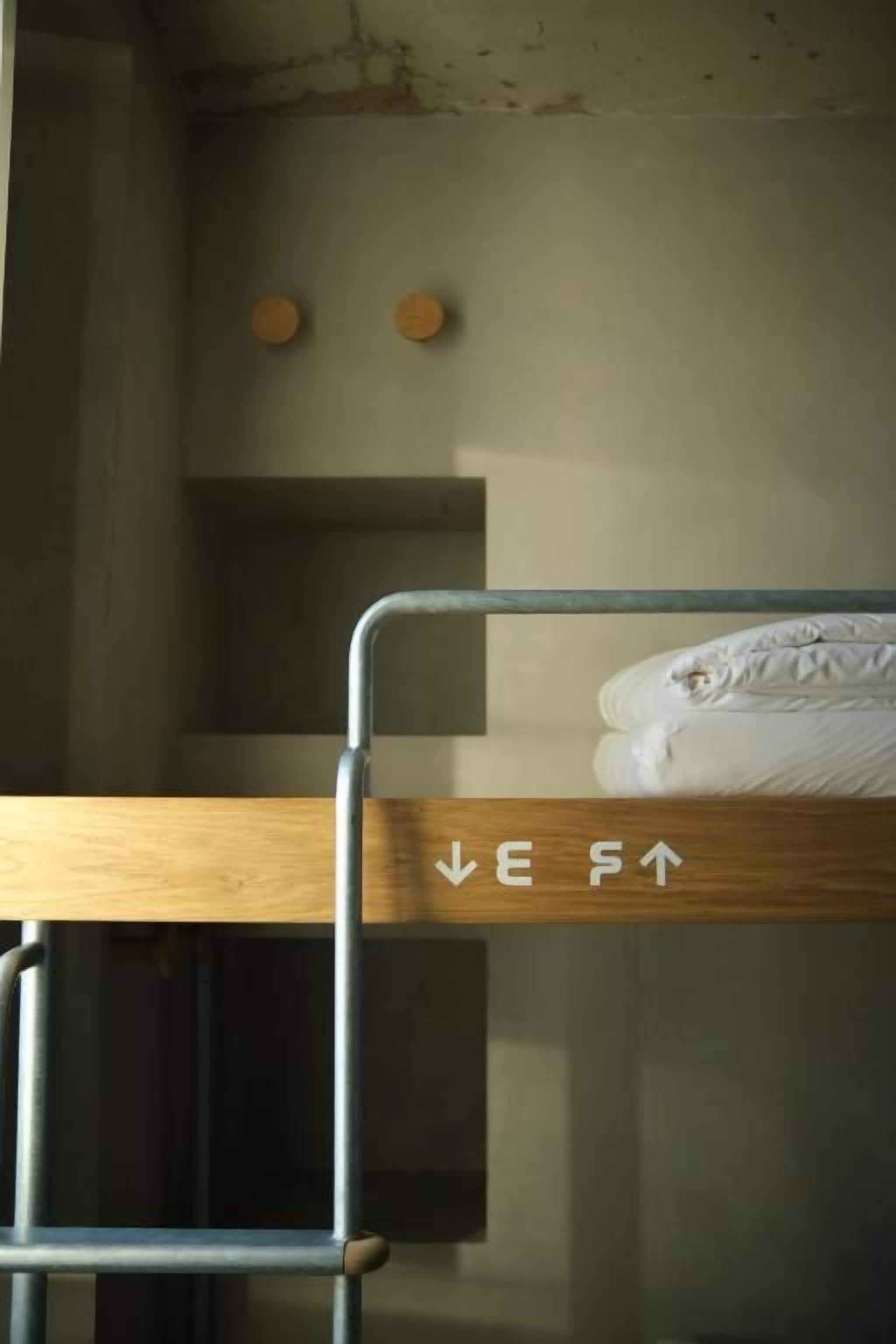 Un lit superposé avec une structure en bois et des barreaux en métal, un matelas blanc et un mur orné de deux objets circulaires.