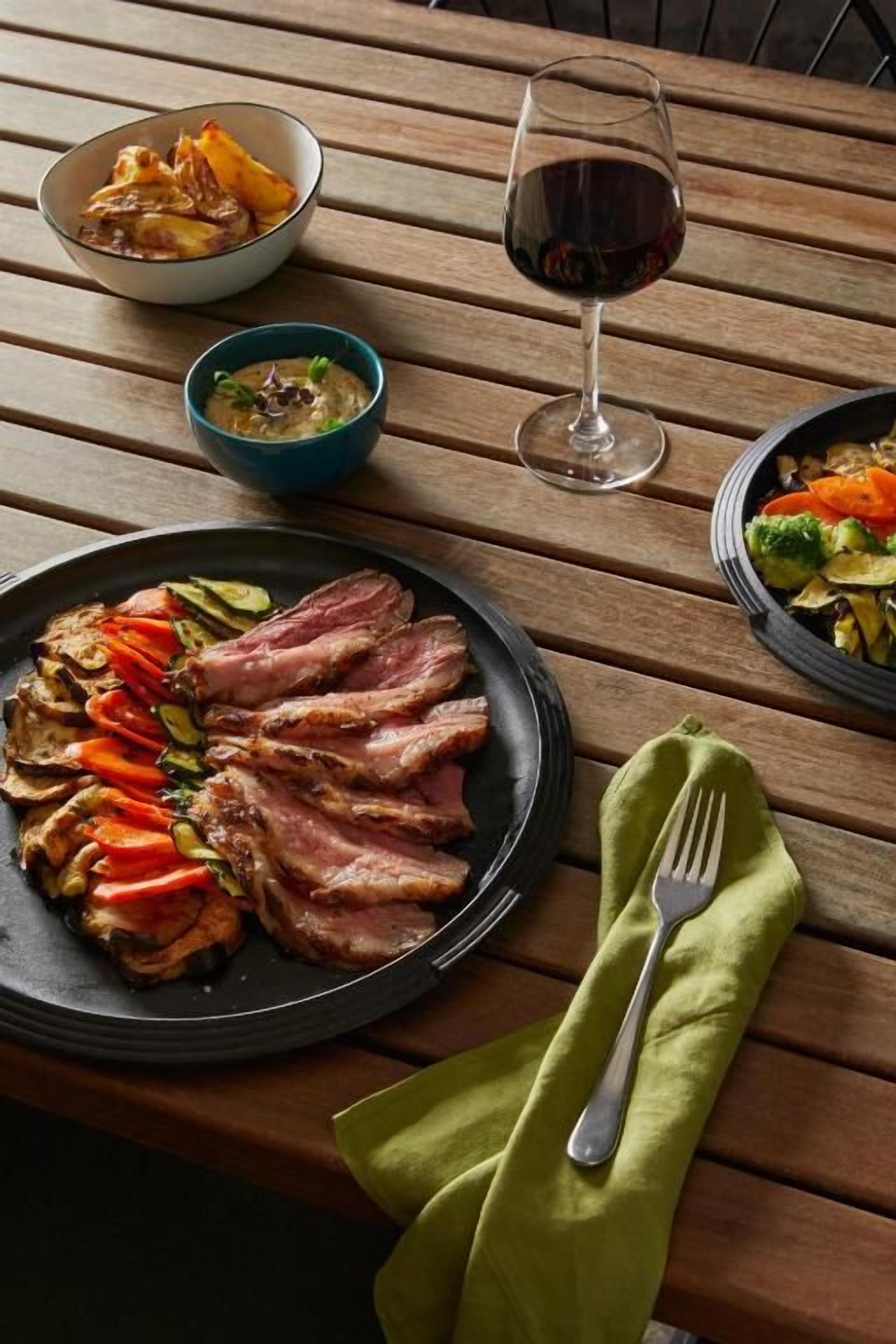 Una mesa de madera con un plato de carne en rodajas, un tazón de sopa y una copa de vino tinto.