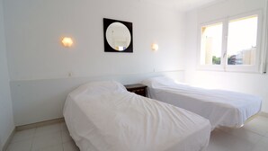 A room with two single beds, a small bedside table, a wall-mounted mirror, and two wall sconces.