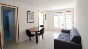 A living room with a sofa, a dining table with chairs, a framed picture on the wall, and a door leading to a bathroom.