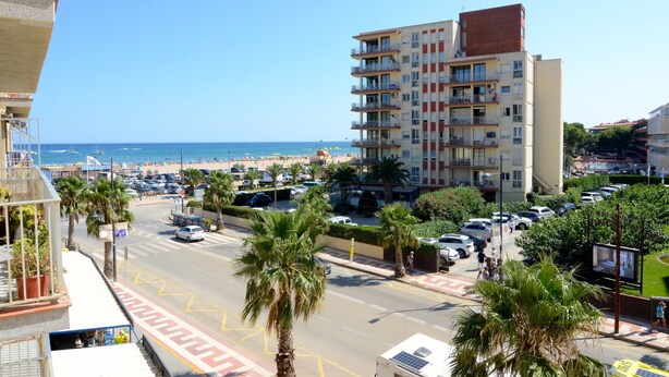 A coastal urban area with a multi-story building, palm trees, and a clear view of the sea.