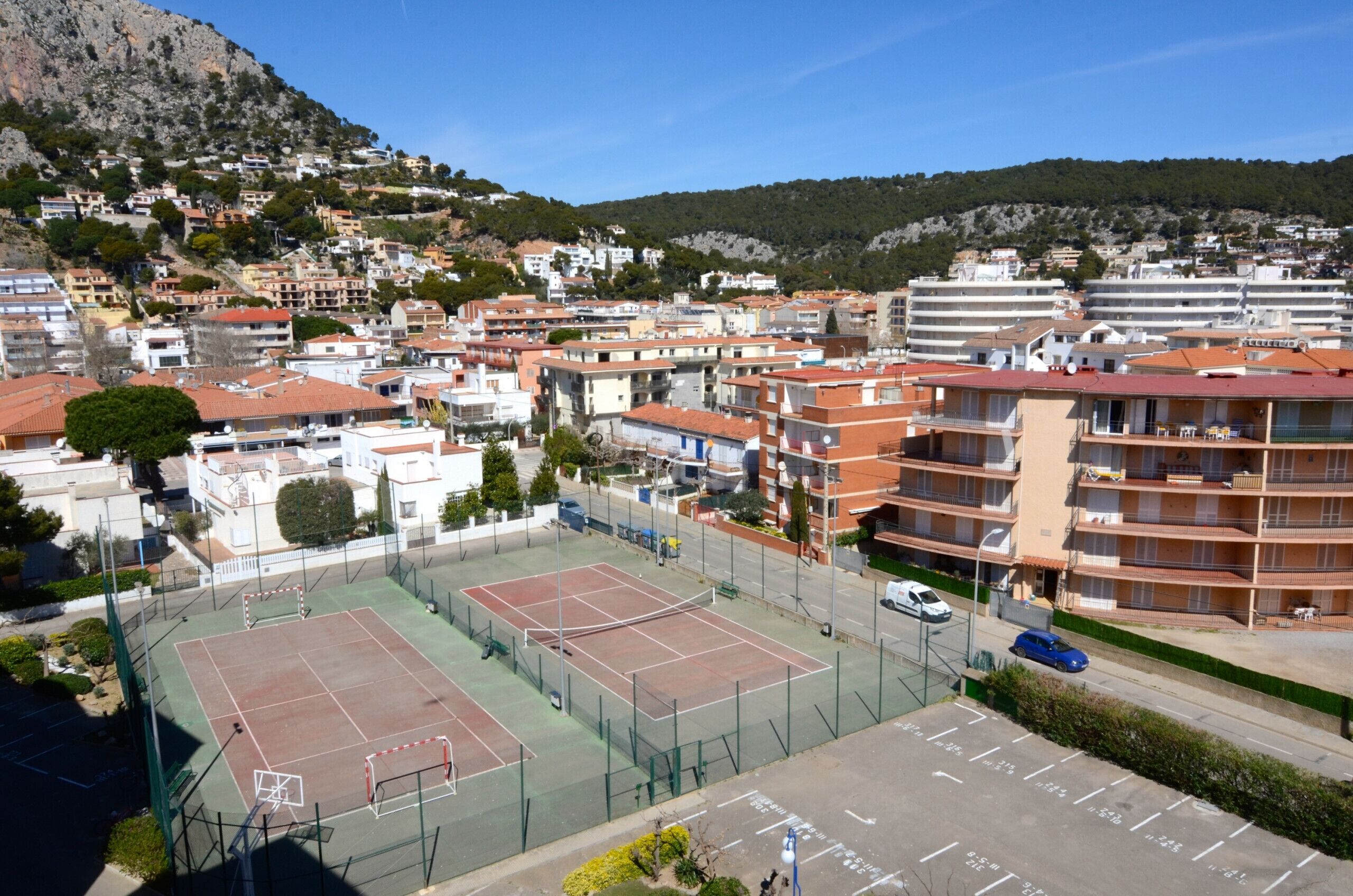 En tenniskort omgiven av bostadshus, med en parkeringsplats i förgrunden.
