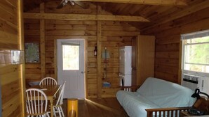A wooden cabin interior with a dining area, a bed, and a window. - Acadia Explorer Cabin Rentals Cabin 1  (Southwest Harbor)