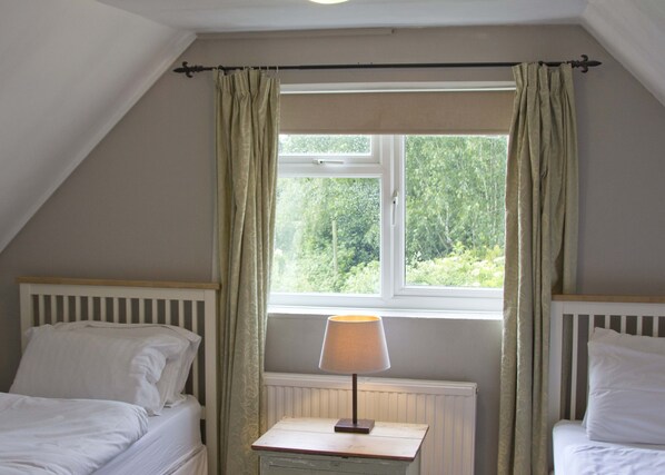 A bedroom with two single beds, a window with curtains, a bedside table with a lamp, and a radiator.