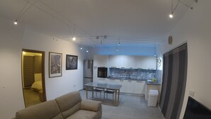 Een moderne woonkamer met een bank, een eettafel en een keuken met kastjes en een koelkast.