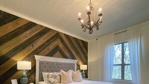 Ein Schlafzimmer mit einem großen Bett, einer Chandelüster, einem Nachttisch und einem Fenster mit Vorhängen.