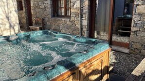 A stone building with a spa area including a hot tub and a wooden deck.