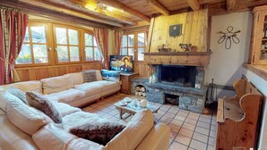 A cozy cabin interior with a stone fireplace, wooden beams, a sofa, and a television.