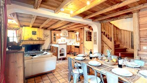 A rustic interior with a dining area, wooden beams, and a fireplace.