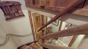 A wooden staircase with a rustic design, a wooden shelf with kitchen utensils, and a door with a decorative panel.
