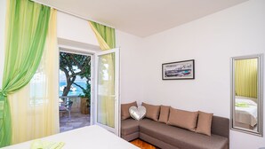 A room with a sofa, a heart-shaped pillow, a framed picture, and a view through a glass door. - Apartments Nikolina (LU) - Two-Bedroom Apartment with Terrace (Lumbarda)