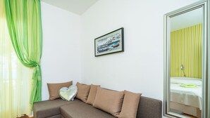 A modern living room with a sectional sofa, a framed picture on the wall, and a large mirror reflecting a bed with green bedding. - Apartments Nikolina (LU) - Two-Bedroom Apartment with Terrace (Lumbarda)