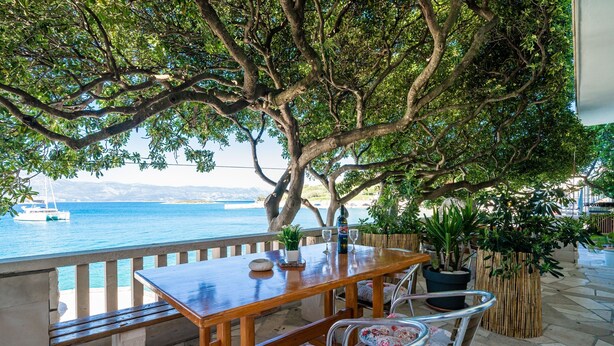 A wooden table with chairs, a potted plant, and a bottle on a terrace overlooking a body of water. - Apartments Nikolina (LU) - Two-Bedroom Apartment with Terrace (Lumbarda)