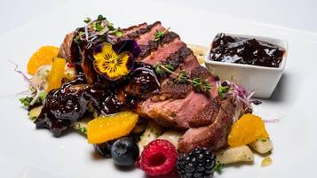 A plate of food with sliced meat, fruits, and a small bowl of sauce.