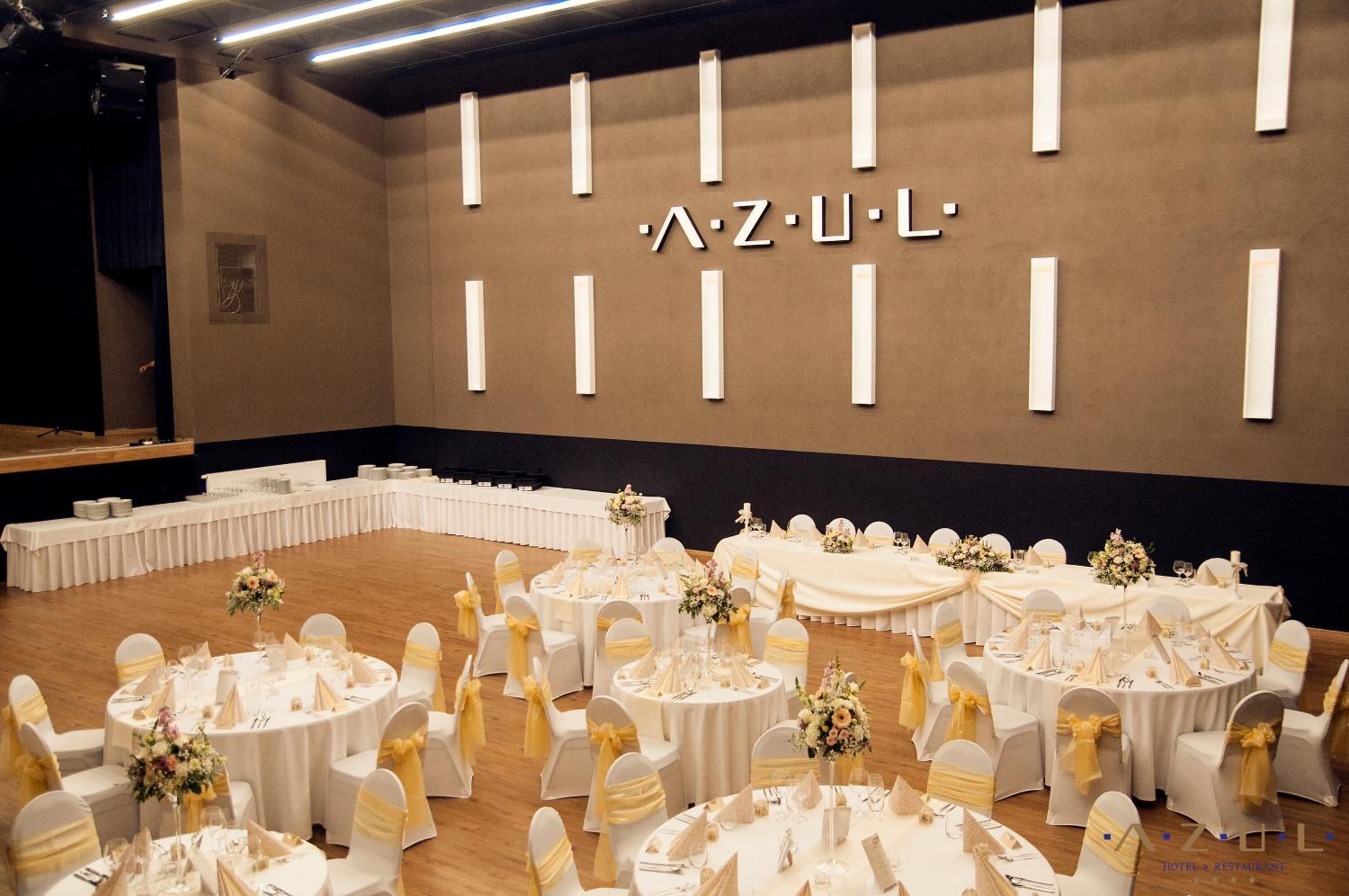 A banquet hall with round tables set for a formal event, featuring white tablecloths and gold sashes.