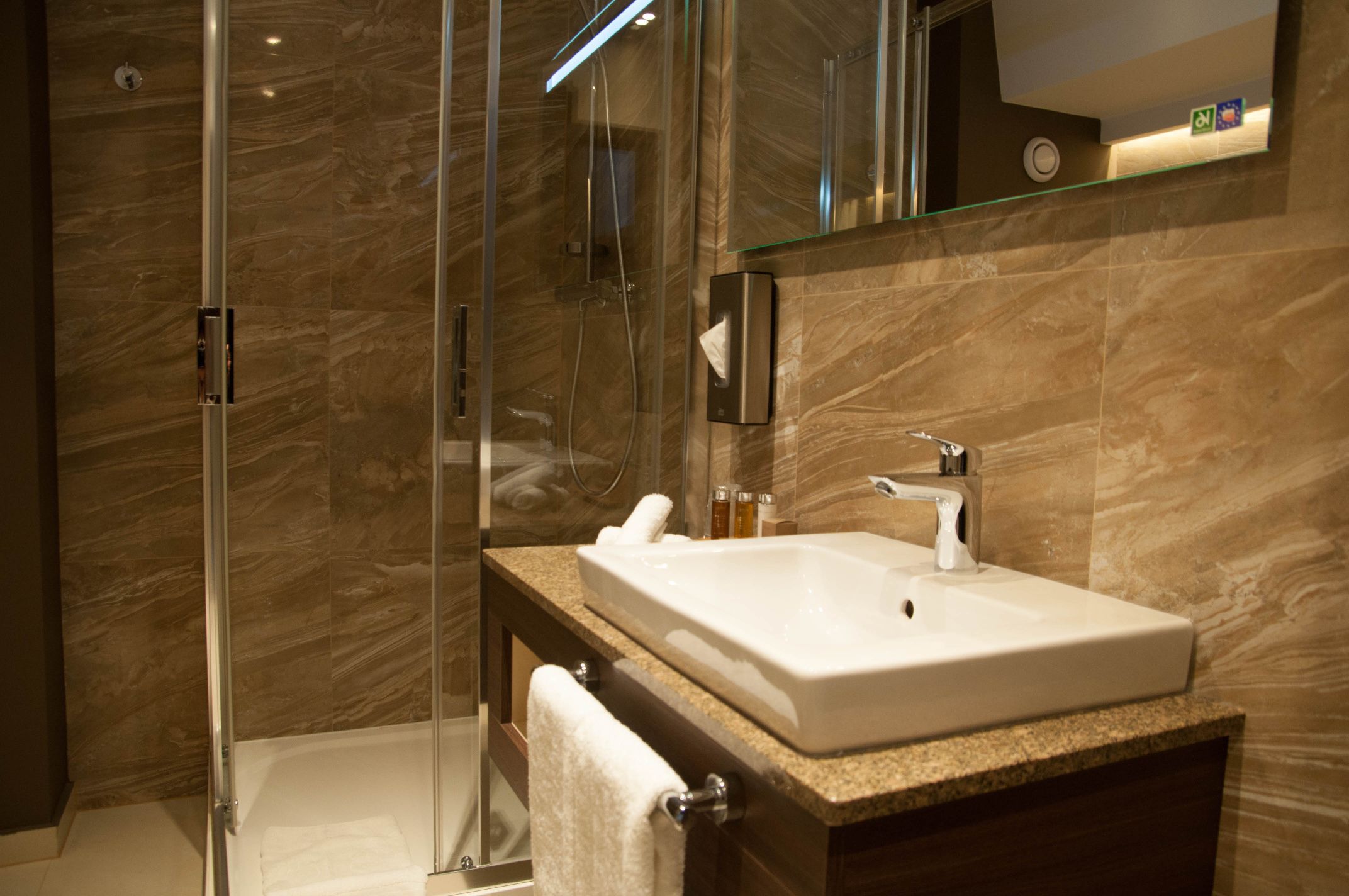 A modern bathroom with a glass-enclosed shower, a white sink, and a marble-tiled wall.