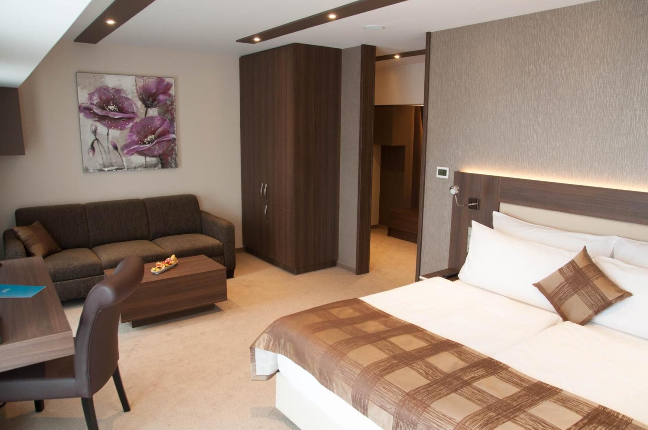 Ein modernes Hotelzimmer mit einem großen Bett, einer Couch, einem Esstisch und einem Blumenbild an der Wand.
