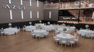 A spacious hall with multiple round tables set for events, a staircase, and a modern design with a dark wall and white accents.