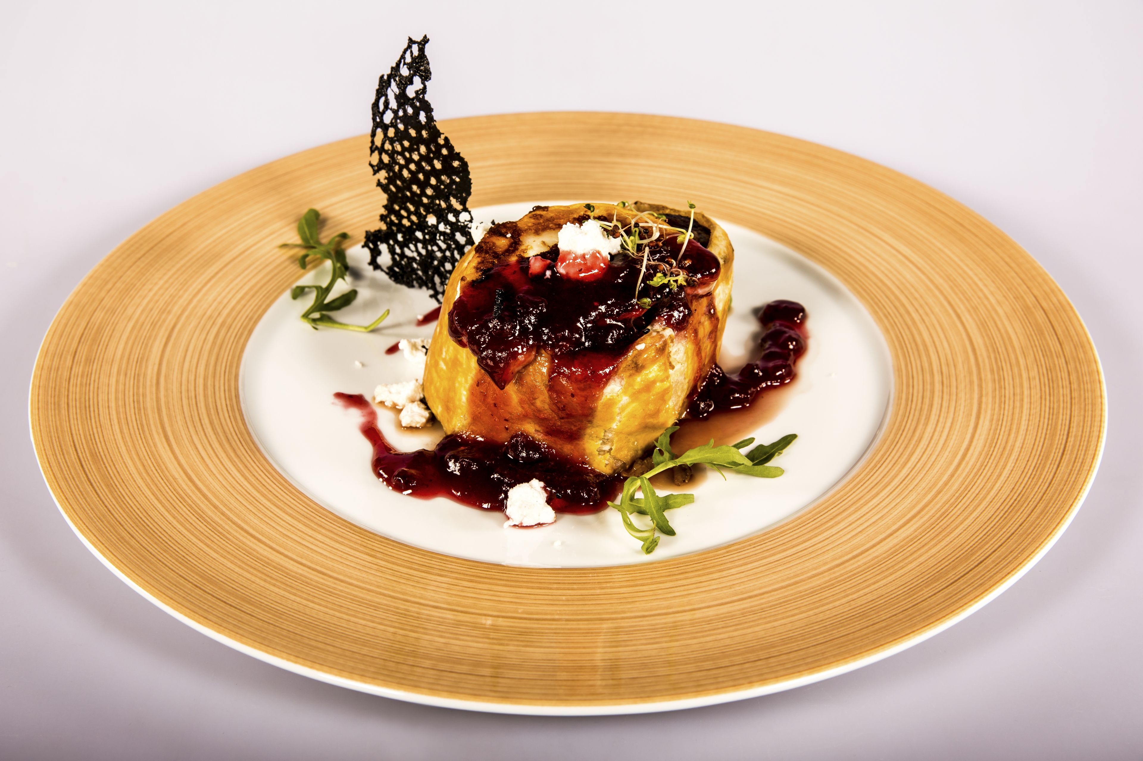 Un postre en un plato con una hoja decorativa y salsa de frutos rojos.