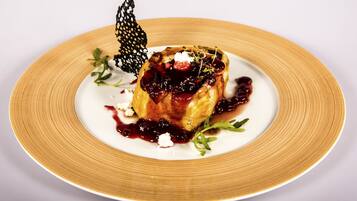 Un postre en un plato con una hoja decorativa y salsa de frutos rojos.