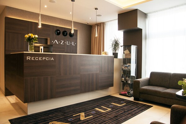 A modern reception area with a dark wood finish, a reception desk labeled "RECEPCIA," and a "ZULU" rug on the floor.