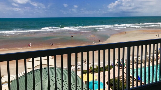 Vue sur la plage depuis un balcon donnant sur une piscine et un espace de détente.