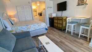 Un espace de vie compact comprenant un canapé, une petite table, un lit, une kitchenette et un téléviseur fixé au mur.