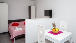 A bedroom with a bed, a TV, a wardrobe, and a small dining area with a table and chairs. - Villa Roza - Studio Apartment with Balcony (Mokosica)