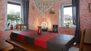 Ein Zimmer mit einem Bett, einem Schreibtisch, einer Vase, einem Lautsprecher und einem Fenster mit Vorhängen.