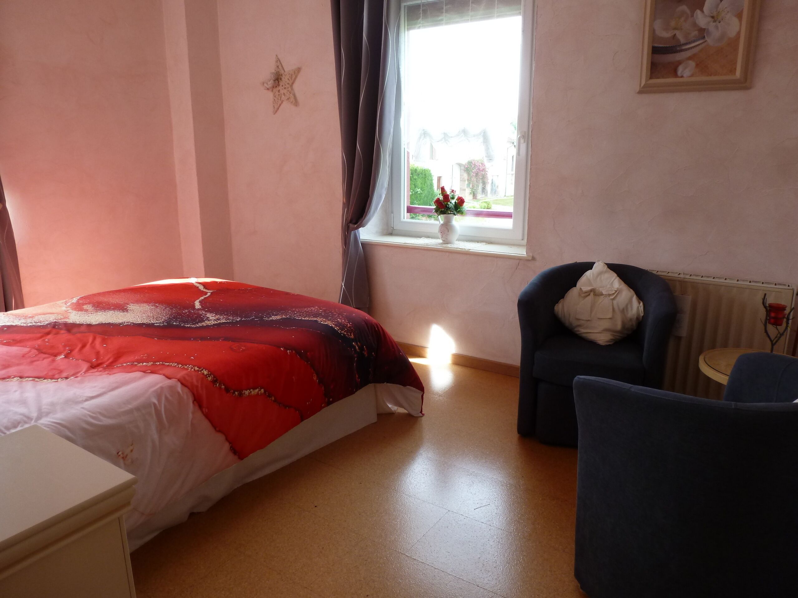 A bedroom with a bed, a chair, a window with a view, and a radiator.