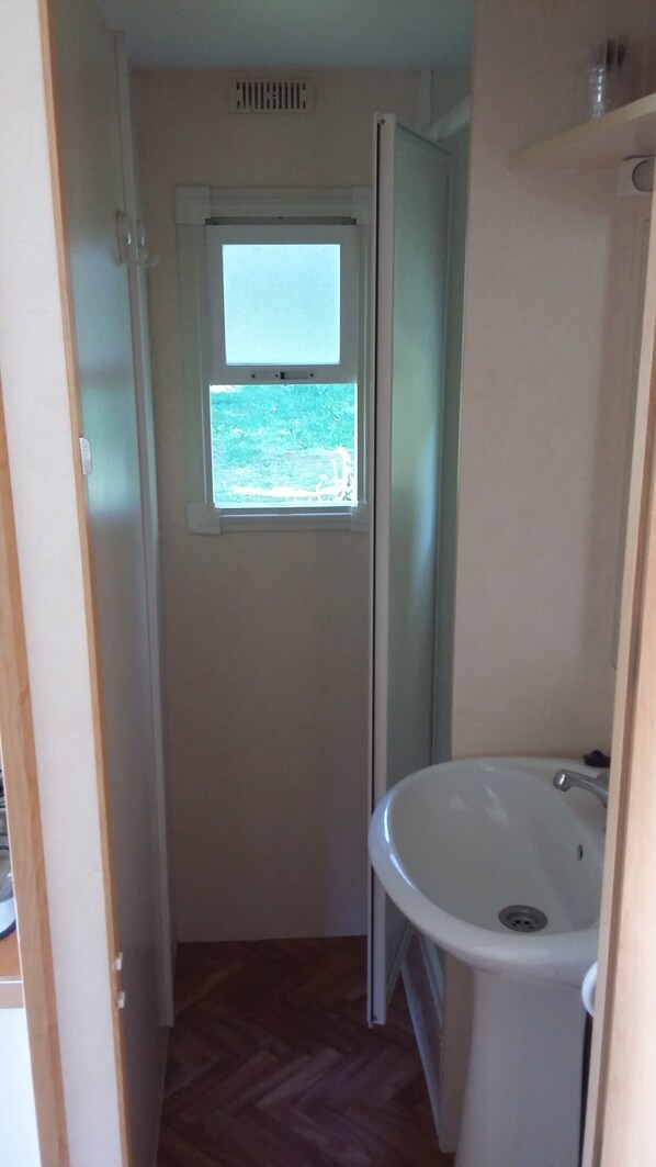 Un baño estrecho con ventana, lavamanos y puerta.