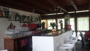 A bar area with shelves of liquor bottles, glasses, and a coffee machine. - Camping de Fléchat (Orcival)