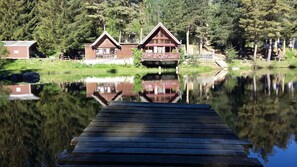 A wooden dock leading to a cabin with a reflection in the water. - Camping de Fléchat (Orcival)
