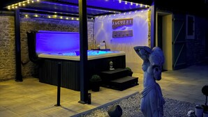 A hot tub under a pergola with string lights, a statue, and a sign reading 'JACUZZI'. - L'Echappee Vendeenne Chambres d'Hotes (Saint-Aubin-la-Plaine)