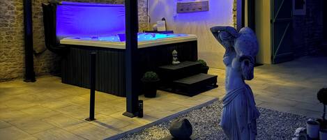 A hot tub under a pergola with string lights, a statue, and a sign reading 'JACUZZI'.