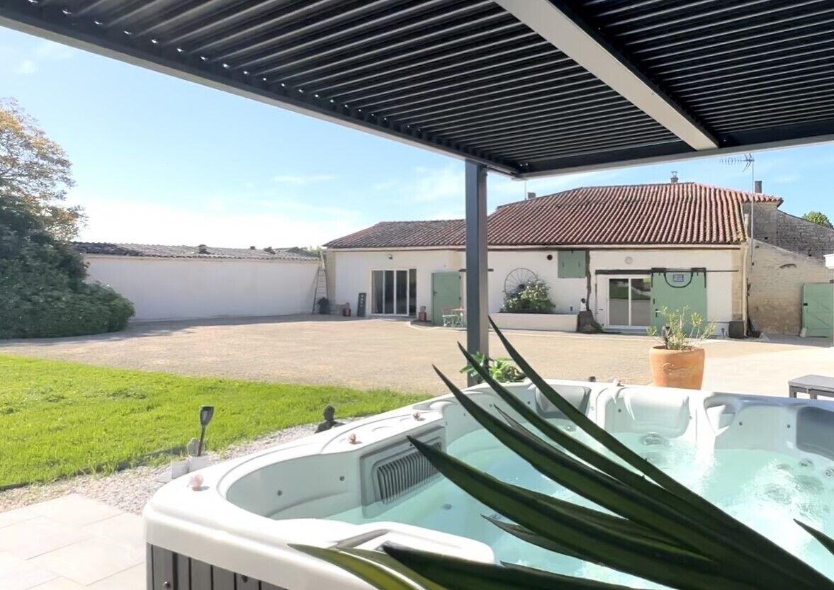 A hot tub under a pergola with a view of a house and a grassy area.