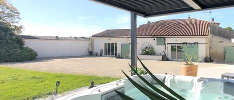 Ett bubbelbad under en pergola med utsikt över ett hus och en gräsyta.
